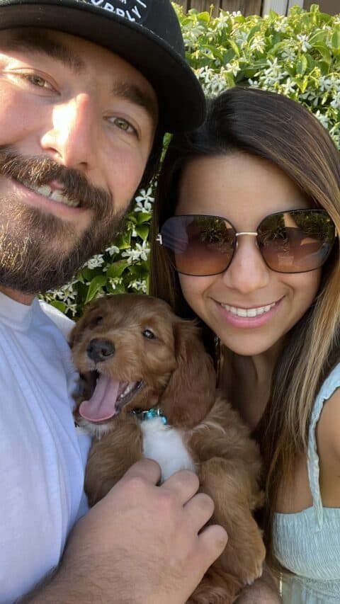 Husband and wife posing with their new Goldendoodle puppy