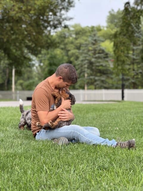 Man playing with a small goldendoodle puppy in the yard