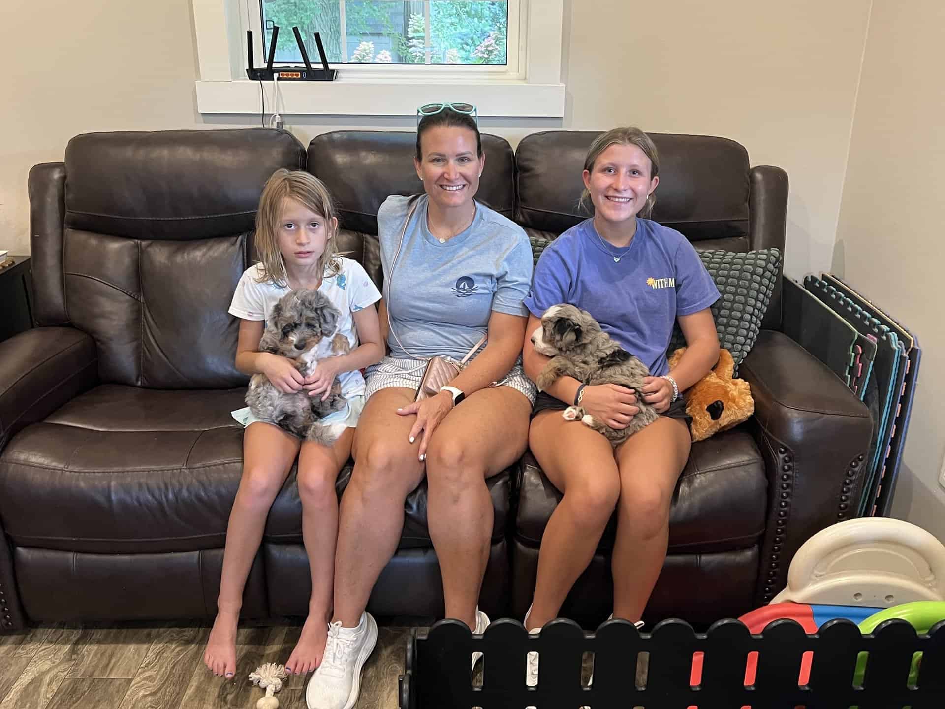 A mom with her two daughters each holding a puppy on a couch at Fawn River Doodles