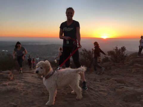 Athletic woman posing with puppy on a mountain with a sunset in the background